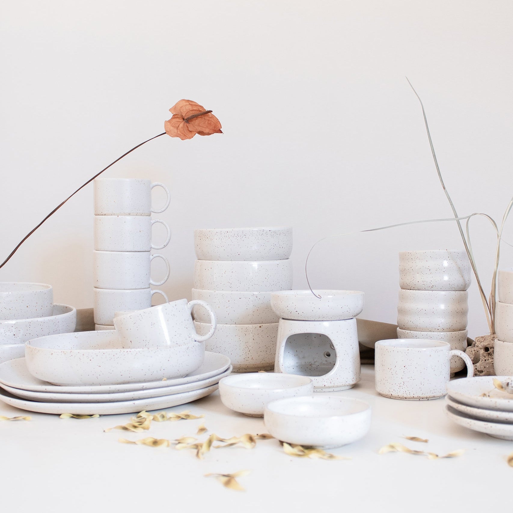 An assortment of artisanal tableware by Made of Dust Ceramics, crafted in speckled white finish, arranged against white backdrop.