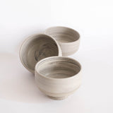 Three handmade earthy-toned ice cream bowls scattered on a white background.