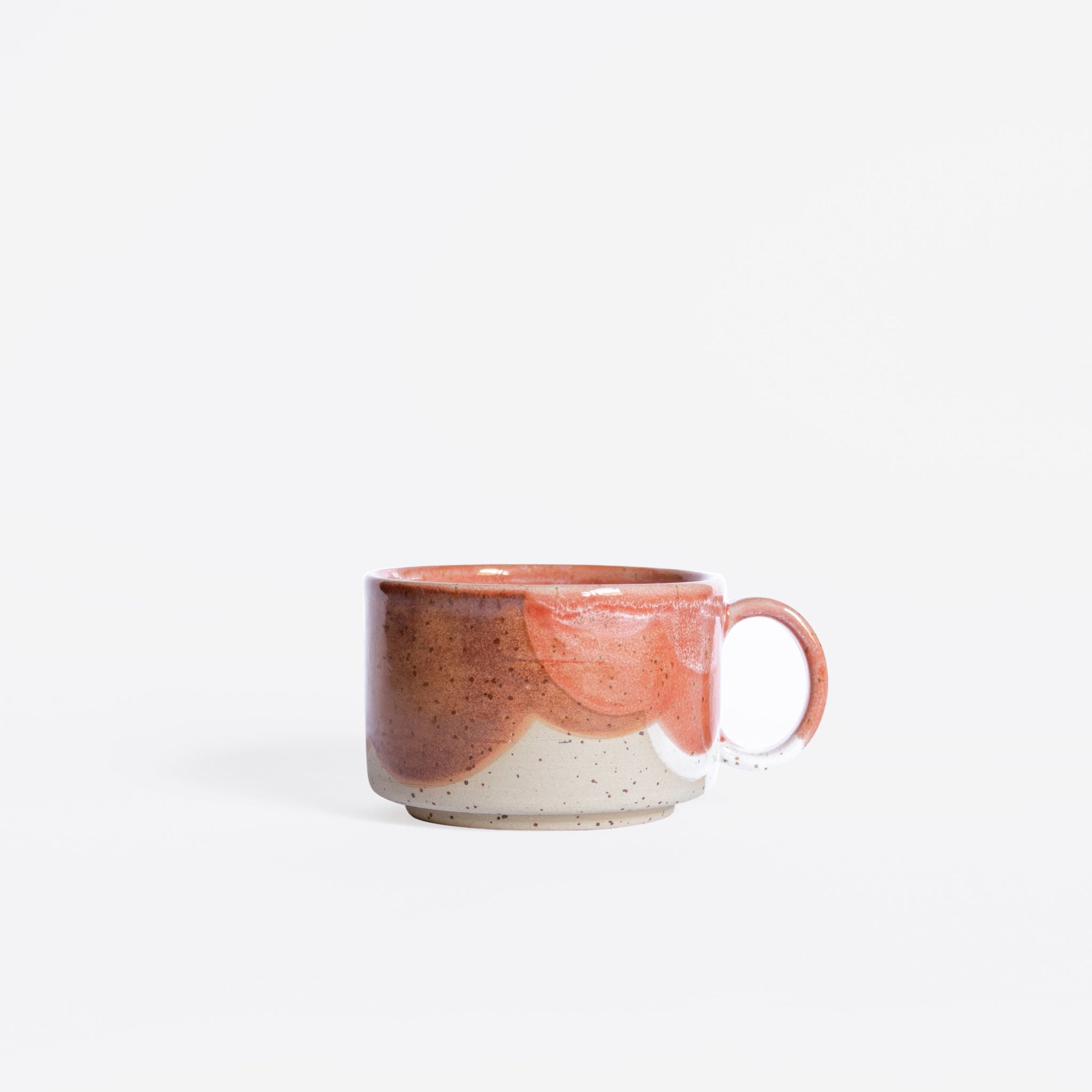 A handcrafted ceramic cup with a handle, displaying a lively organic pattern in coral red and white finishes, showcased against a pristine white background.
