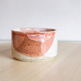 A close-up view of a meticulously handcrafted ceramic cup, showcasing a distinctive melting glaze detail in coral red and white.