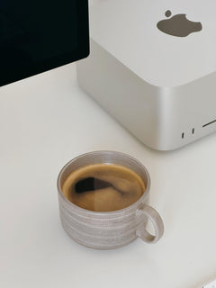 Handmade gray ceramic mug placed on a white table next to a computer monitor.