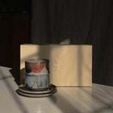 A stack of two ceramic cups on two matching saucers beside a cream-colored Special Occasion Gift Box, lit by dramatic sunlight and strong shadows.