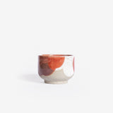 Handmade ceramic cappuccino cup crafted from speckled cream clay, adorned with an organic coral red and white glaze pattern, captured against a white backdrop.