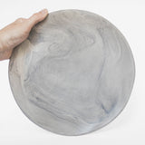 A handmade ceramic plate in gray with a matte marble finish, held against a white background.