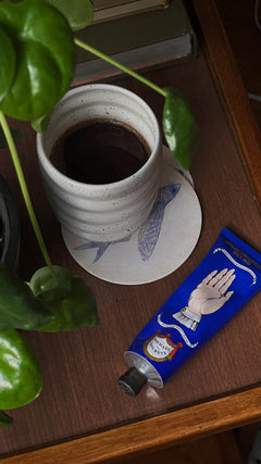 Black coffee served in a handmade ceramic Ripple Speckled White cup by Made of Dust Ceramics, on a wooden table surrounded by house plants.