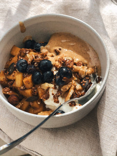 Granola with blueberries served in a handmade ceramic bowl on a linen tablecloth.