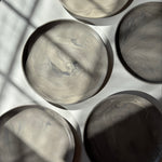 Overhead view of handmade ceramic plates with a matte marble finish, arranged on a white surface where sunlight creates dramatic shadow play.