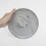 A handmade ceramic plate in gray with a matte marble finish, held against a white background.