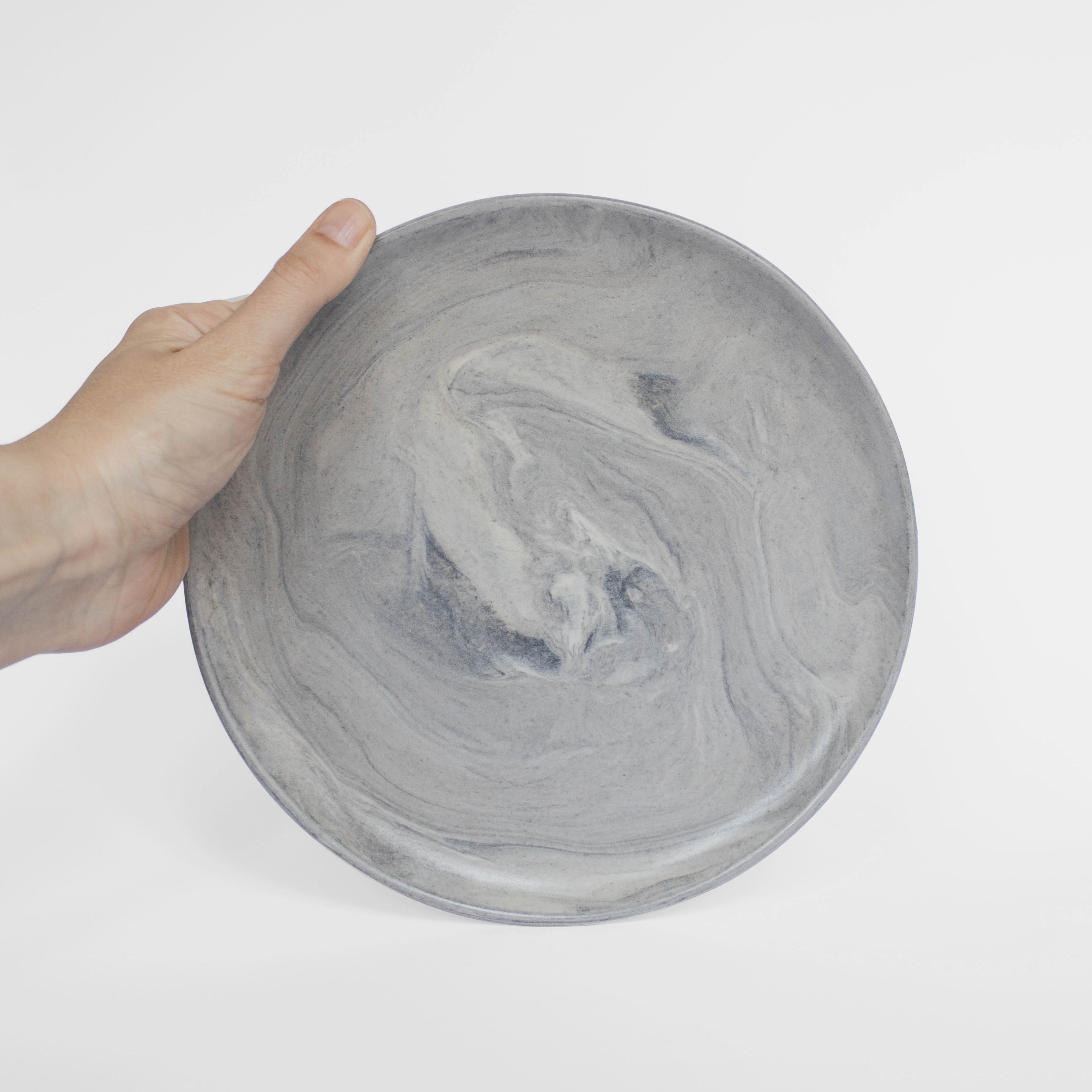 A handmade ceramic plate in gray with a matte marble finish, held against a white background.
