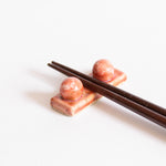 Handcrafted coral red chopstick rest with wooden chopsticks displayed on a white surface.